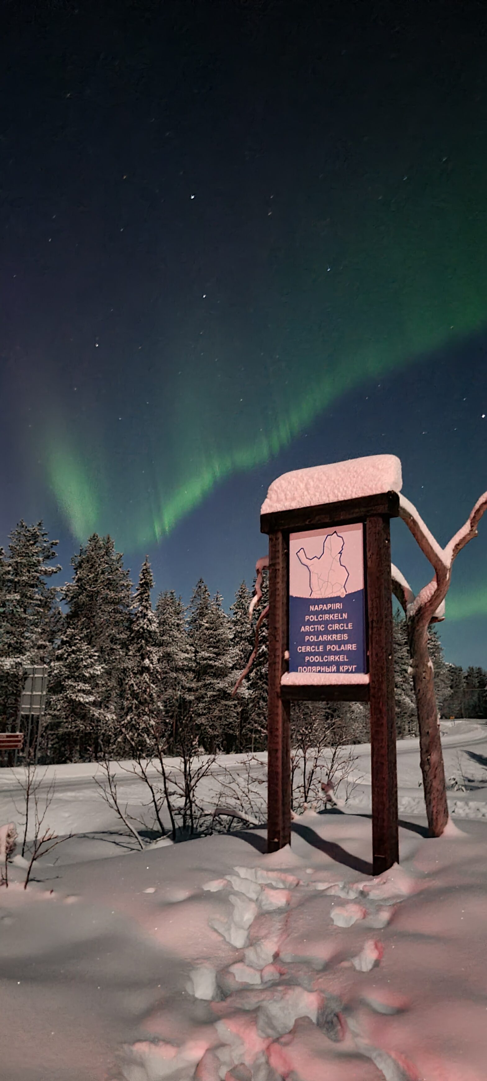 A sign marking the Arctic Circle in Salla, Lapland. The Aurora Borealis can be see in the sky behind.