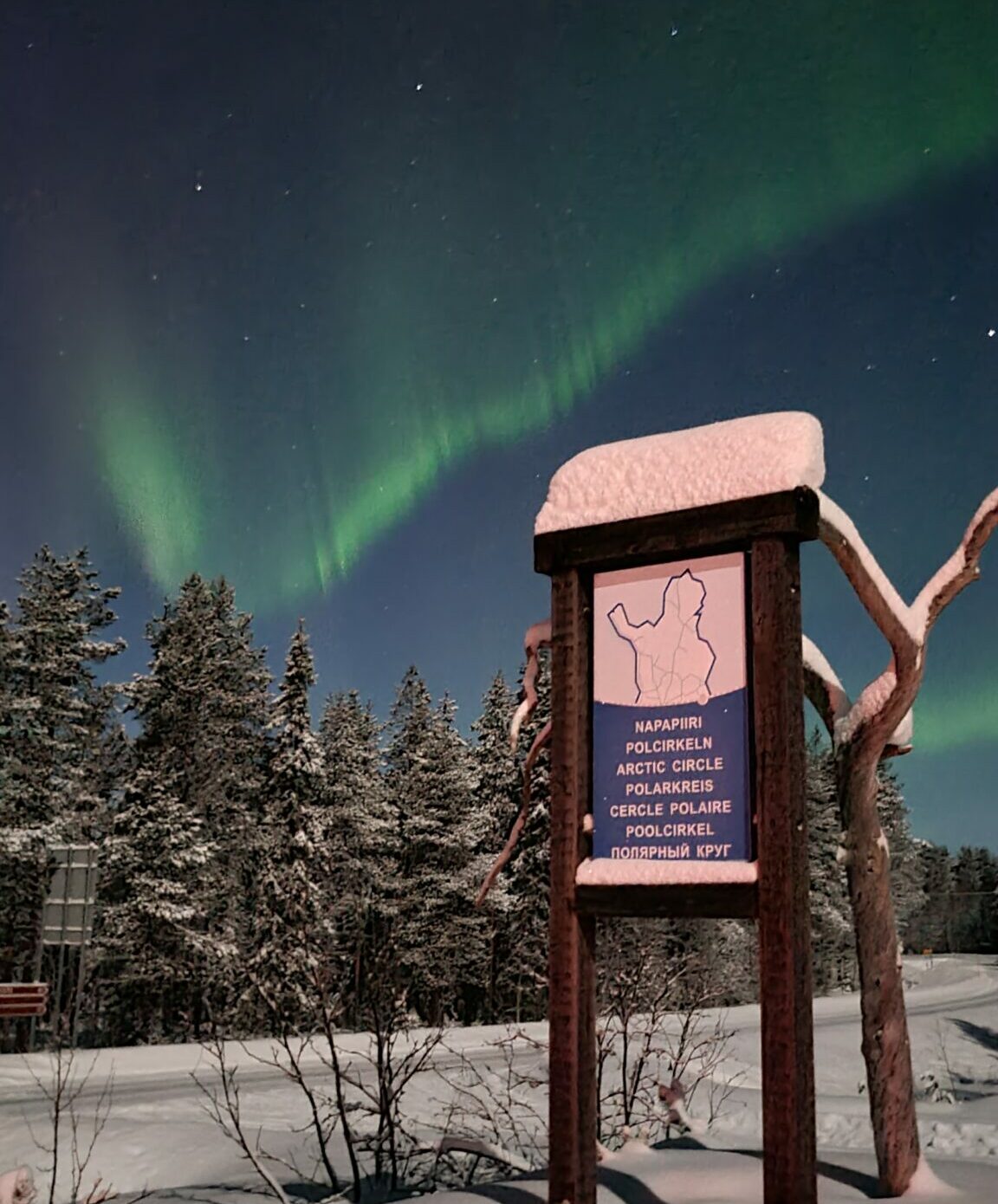 A sign marking the Arctic Circle in Salla, Lapland. The Aurora Borealis can be see in the sky behind.