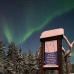 A sign marking the Arctic Circle in Salla, Lapland. The Aurora Borealis can be see in the sky behind.