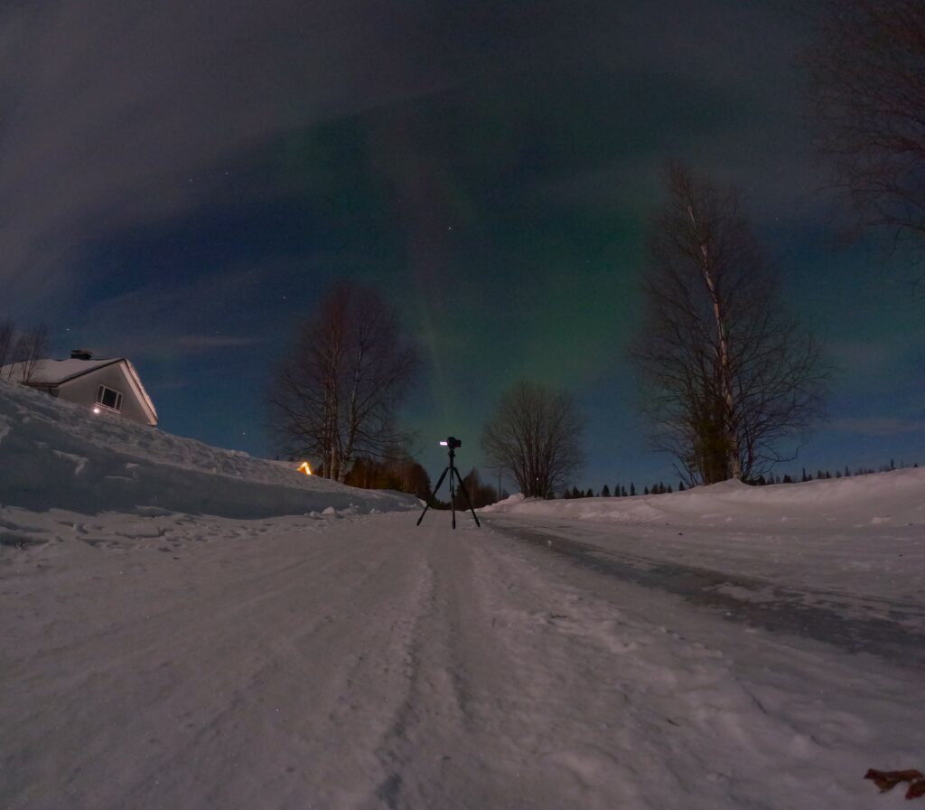 Picture of a camera set up on a tripod and placed on an icy road to take pictures of the northern lights at night in winter.