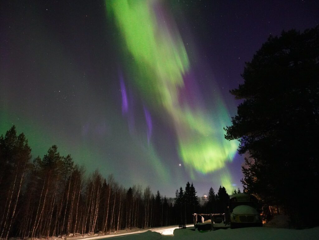 The northern lights dancing over the skoolie conversion in Lapland.